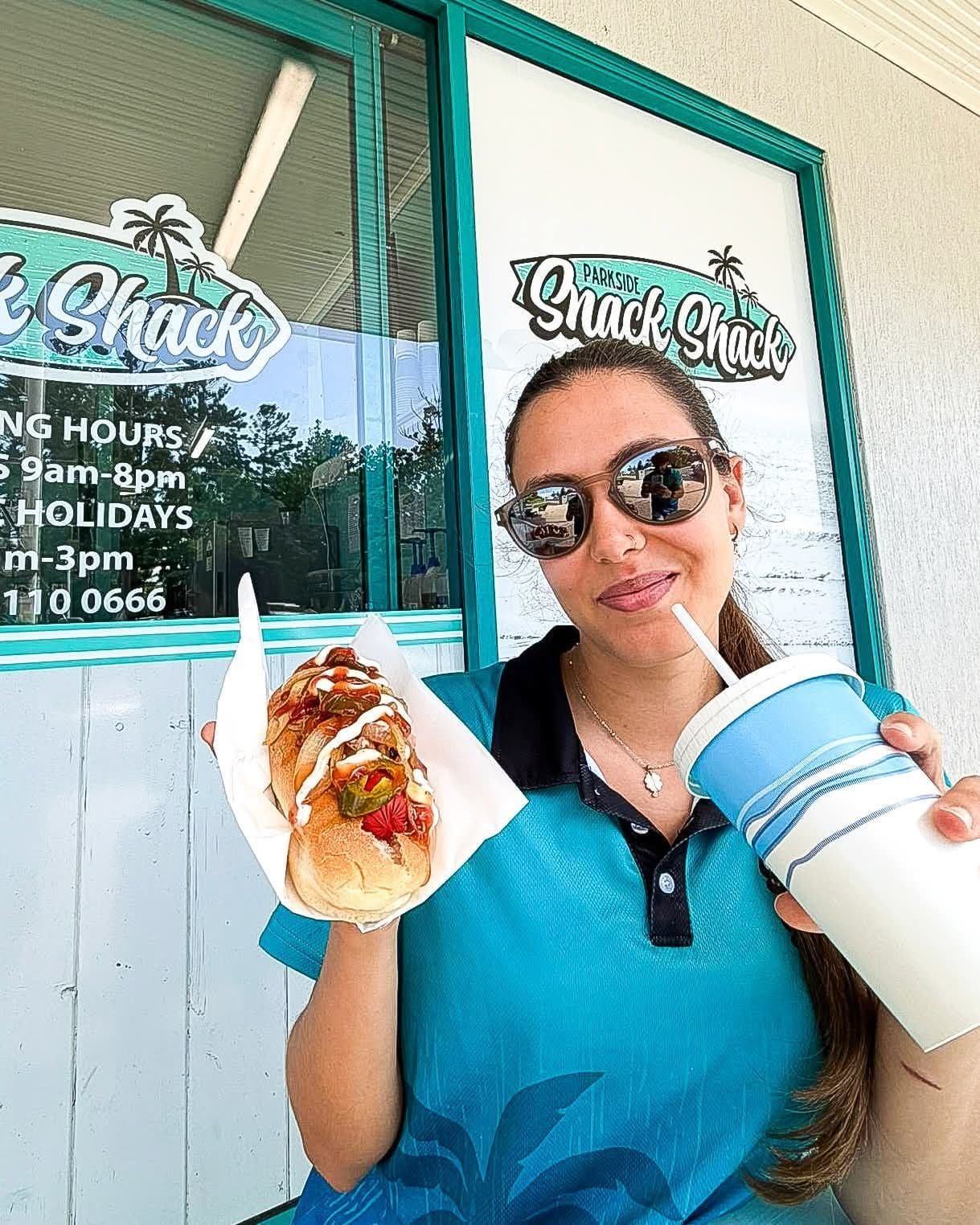 A Parkside Snack Shack team member holding a Chiko roll and a drink at the shop window